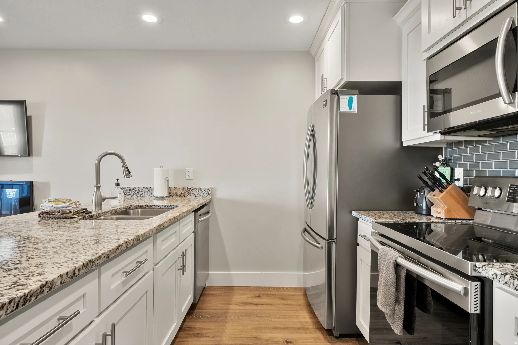 Kitchen featuring white cabinetry, granite-style countertops, wood-finish flooring, recessed lighting, and stainless steel appliances