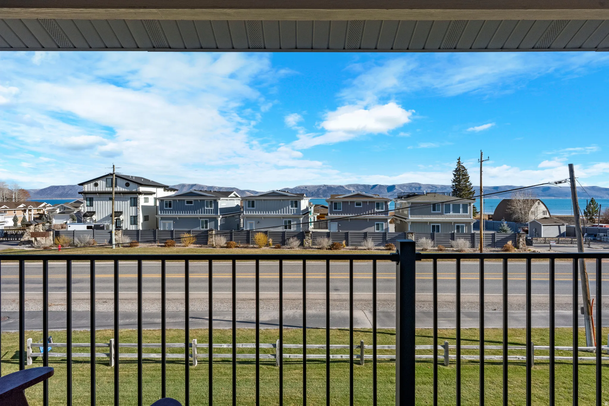 Balcony perspective featuring a black metal railing, overlooking a paved road and a grass lawn