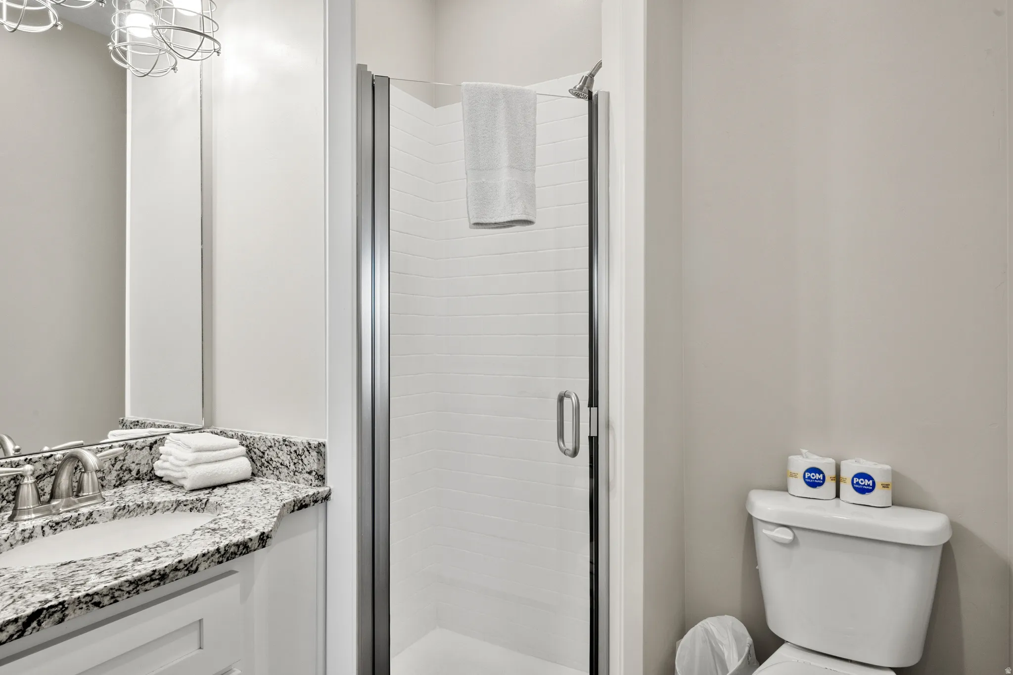 Bathroom featuring a standing shower with a glass enclosure, a vanity with a stone countertop and undermount sink, and a commode