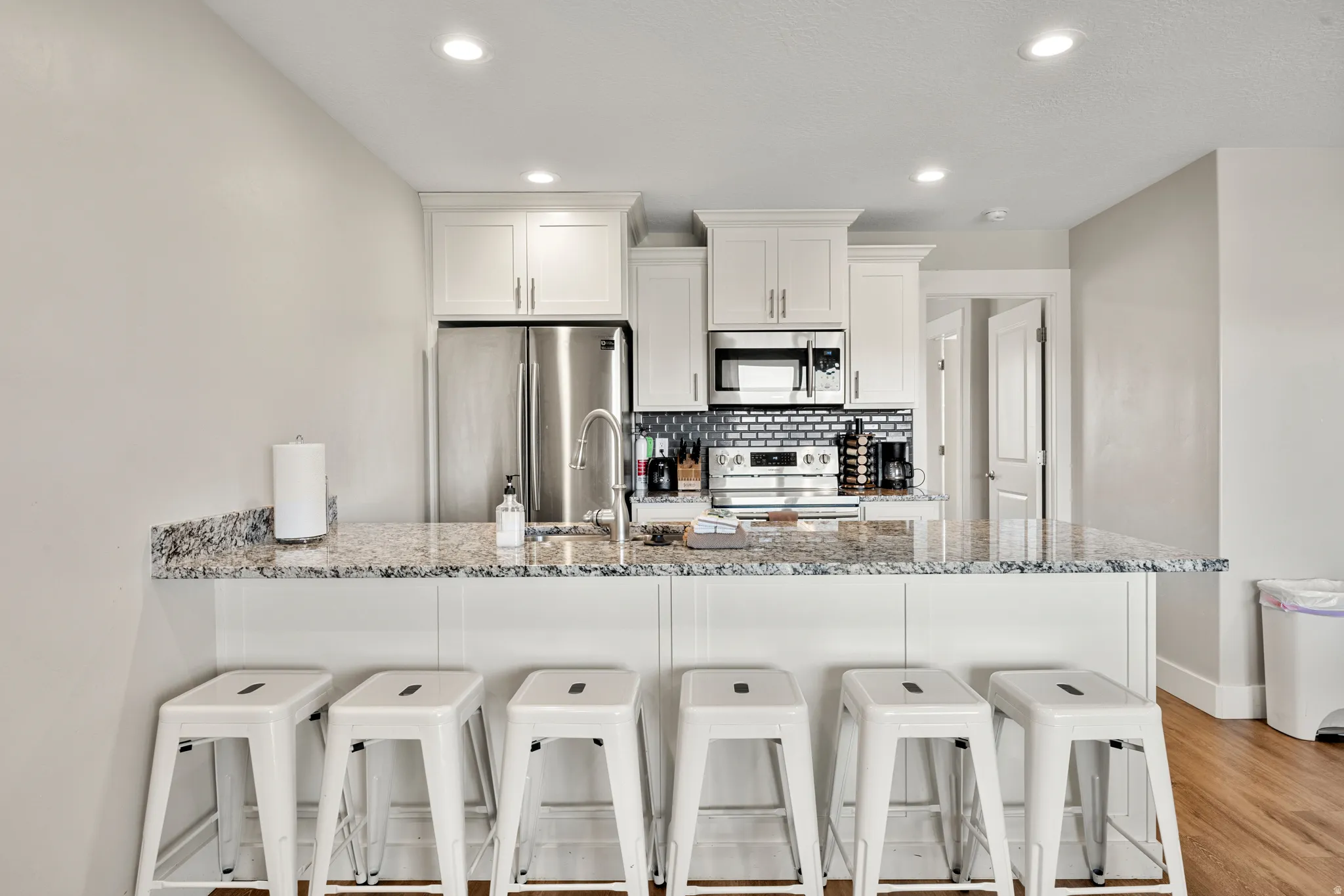 Kitchen featuring a breakfast bar with seating, light-toned cabinetry, stainless steel appliances, a subway tile backsplash, and recessed lighting