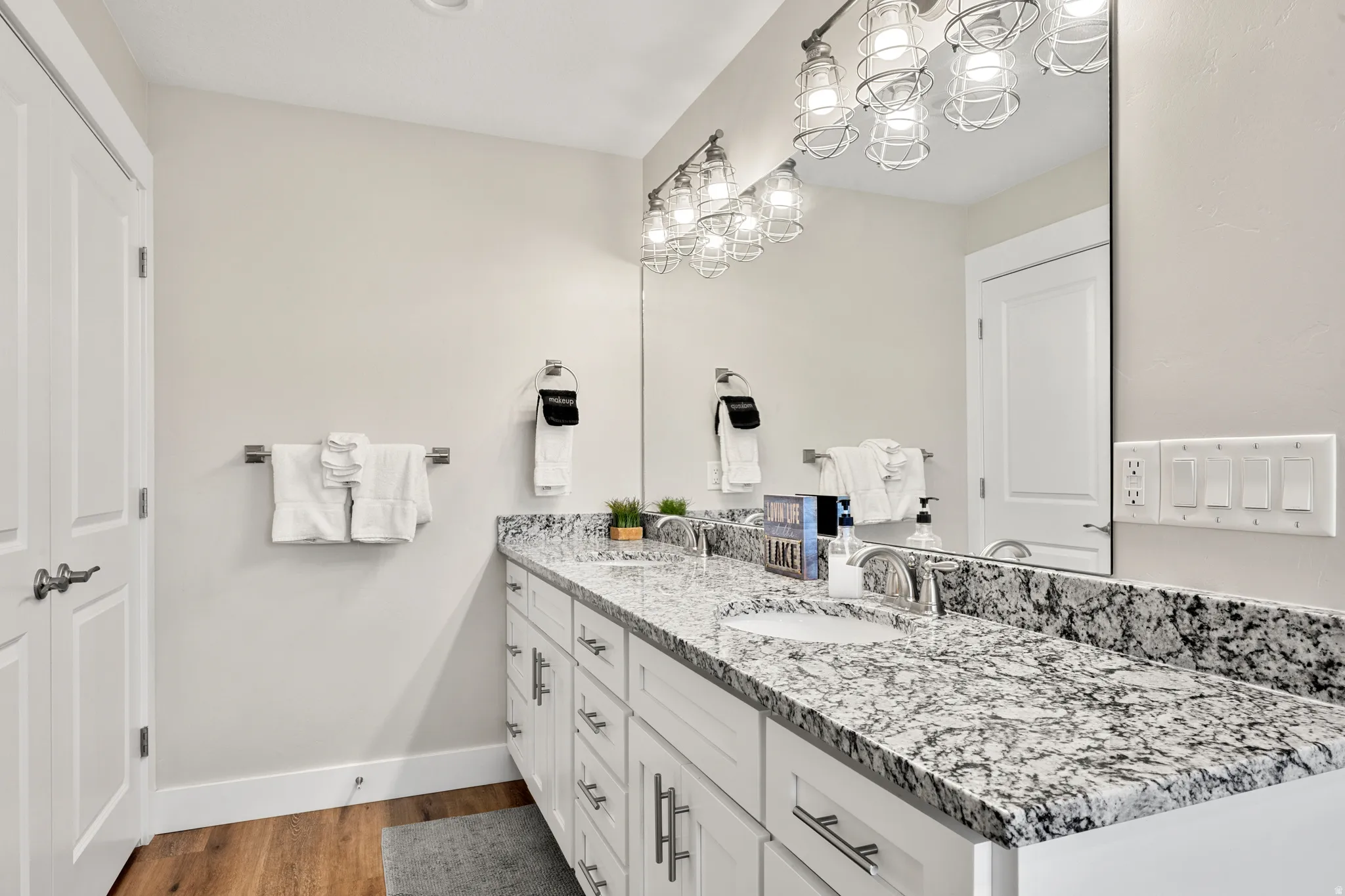 Dual vanity featuring a speckled countertop and undermount sinks, complemented by contemporary cage-style light fixtures and wood-finish flooring