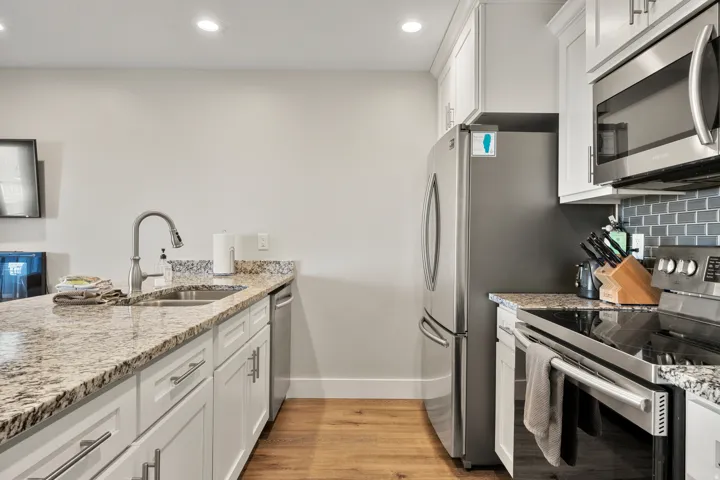 Kitchen featuring white cabinetry, granite-style countertops, wood-finish flooring, recessed lighting, and stainless steel appliances