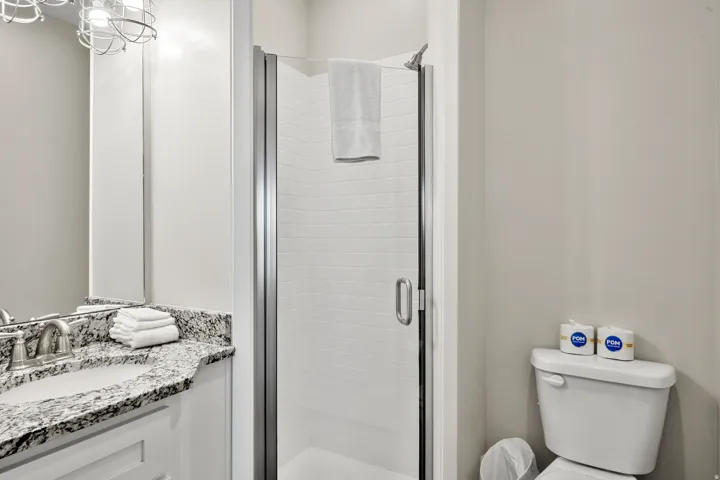 Bathroom featuring a standing shower with a glass enclosure, a vanity with a stone countertop and undermount sink, and a commode