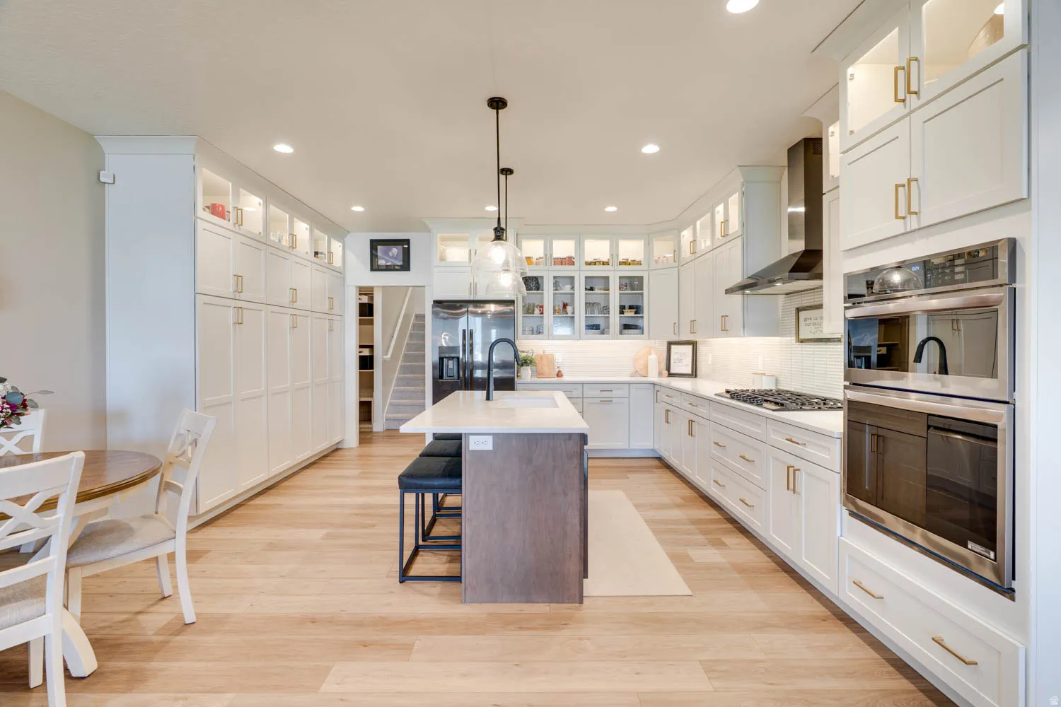 Spacious kitchen featuring an expansive island with seating, a gas cooktop, built-in double ovens, extensive white cabinetry, and wood-finish flooring
