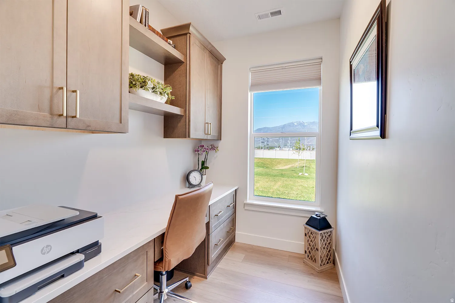Dedicated workspace featuring extensive built-in cabinetry, an integrated desk, light wood-finish flooring, and a large window with mountain scenery