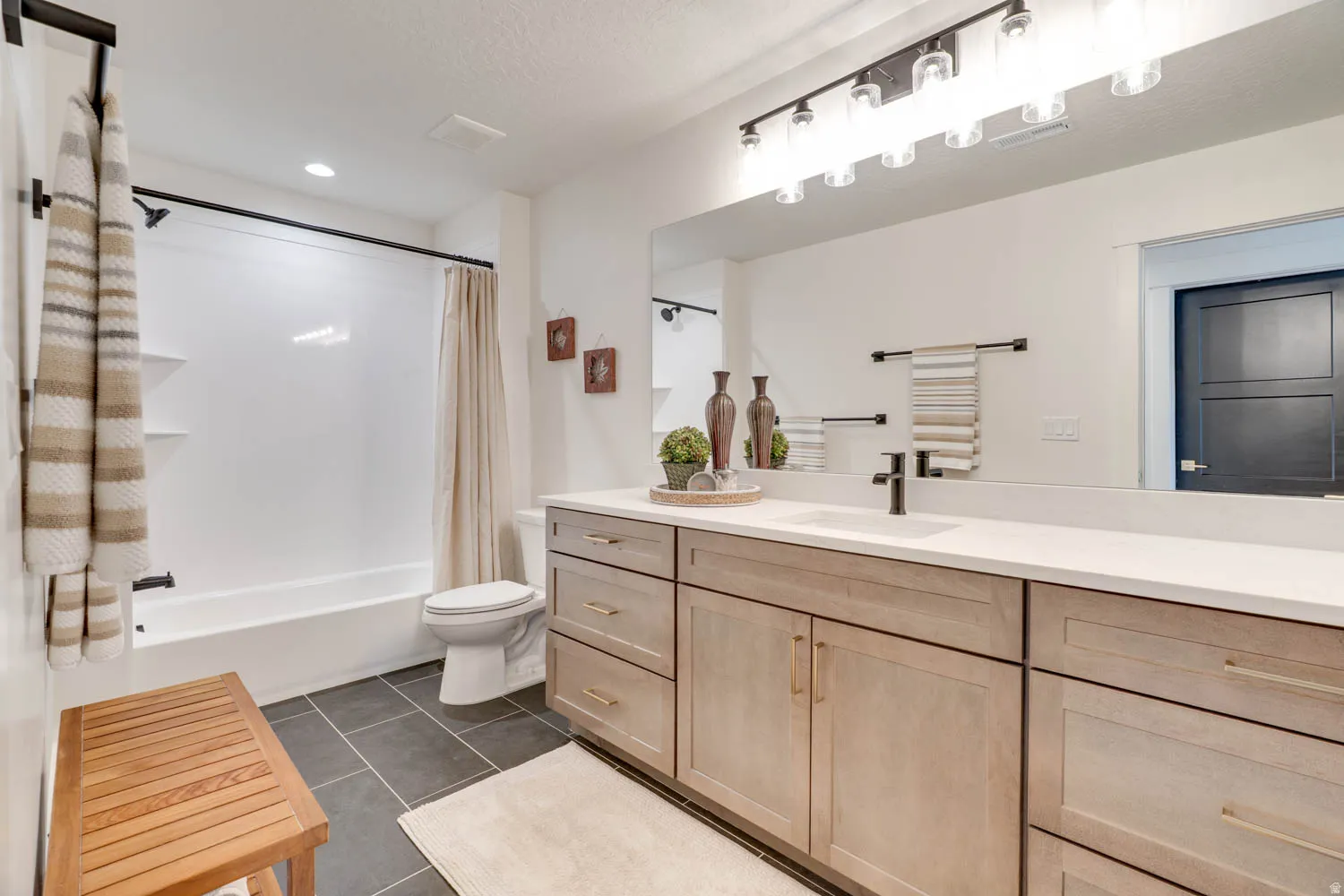 Bathroom featuring a spacious vanity with dual sinks, light wood-finish cabinetry, and a wide countertop