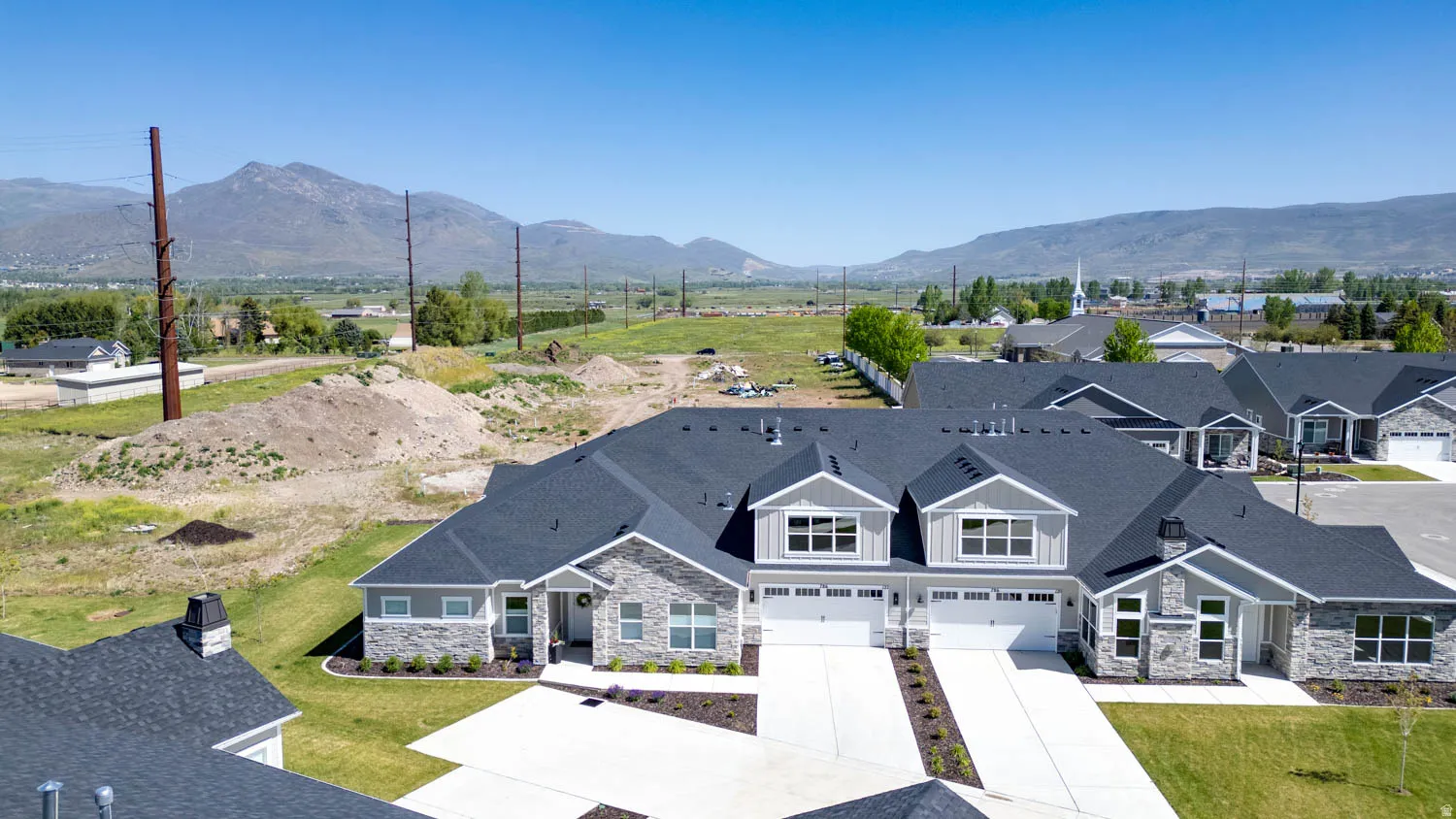 Newly constructed residential complex featuring gray siding with stone accents, dark shingle roofs, and white garage doors