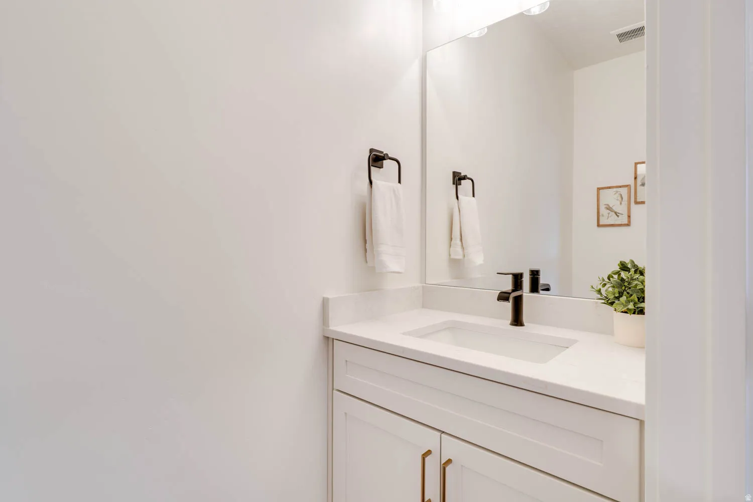 Vanity featuring white shaker-style cabinetry, a white countertop with an integrated rectangular sink, a matte black single-handle faucet, and an oversized wall mirror