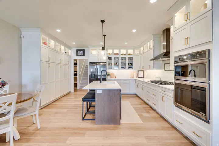 Spacious kitchen featuring an expansive island with seating, a gas cooktop, built-in double ovens, extensive white cabinetry, and wood-finish flooring
