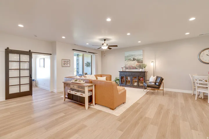 Bright living area featuring light wood-finish flooring, recessed lighting, and a dark-framed sliding barn door with glass panels