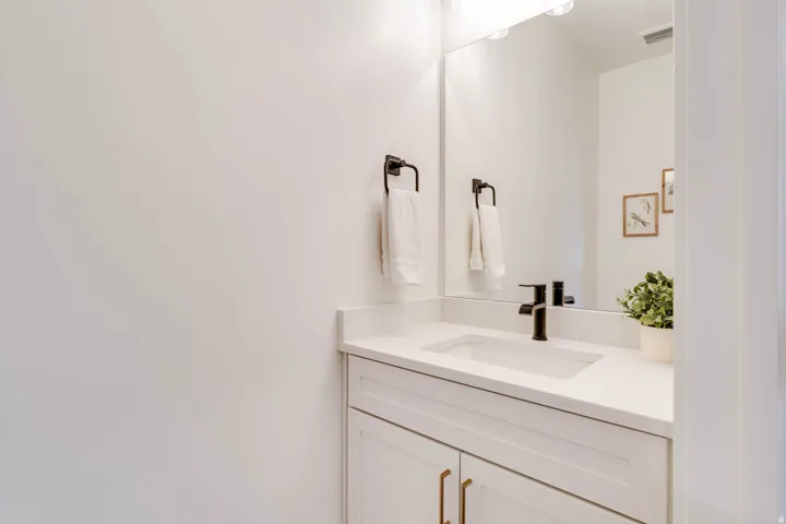 Vanity featuring white shaker-style cabinetry, a white countertop with an integrated rectangular sink, a matte black single-handle faucet, and an oversized wall mirror