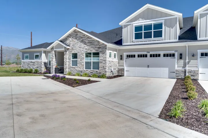 Contemporary townhome featuring a stone and siding exterior, two-car garage with transom windows, a concrete driveway, and mature landscaping