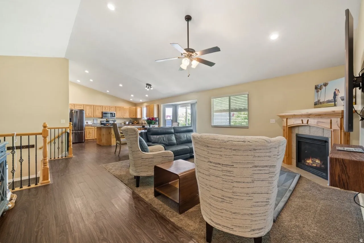 Vaulted ceiling living area featuring wood-finish flooring and a corner gas fireplace with wood mantel
