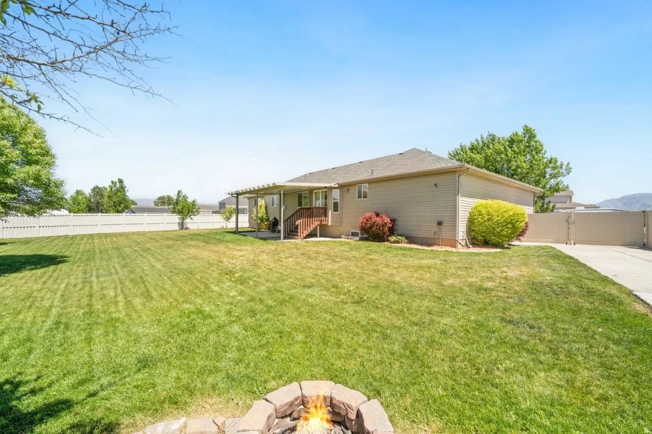 Expansive backyard featuring a stone fire pit, extensive lawn, and white privacy fencing