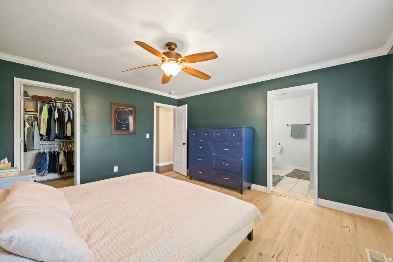 Bedroom featuring wood-finish flooring, a ceiling fan with integrated lighting, and crown molding
