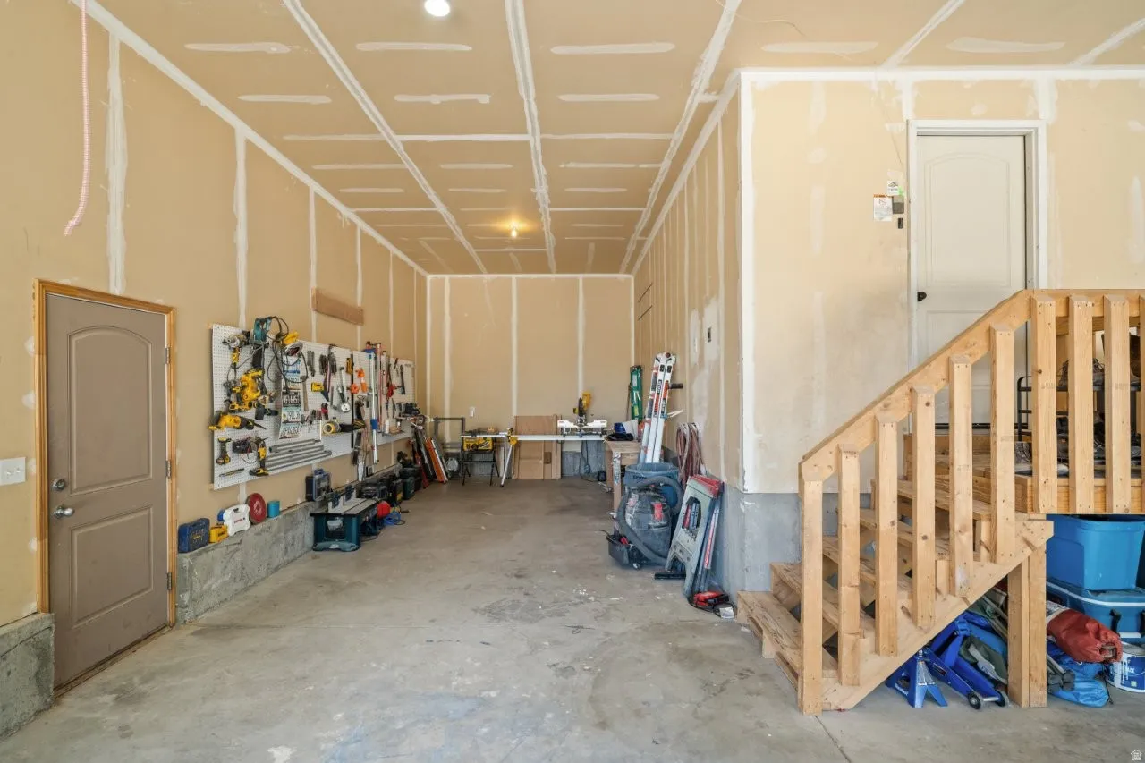 Spacious garage featuring unfinished walls, exposed ceiling joists, a concrete floor, and a wooden staircase