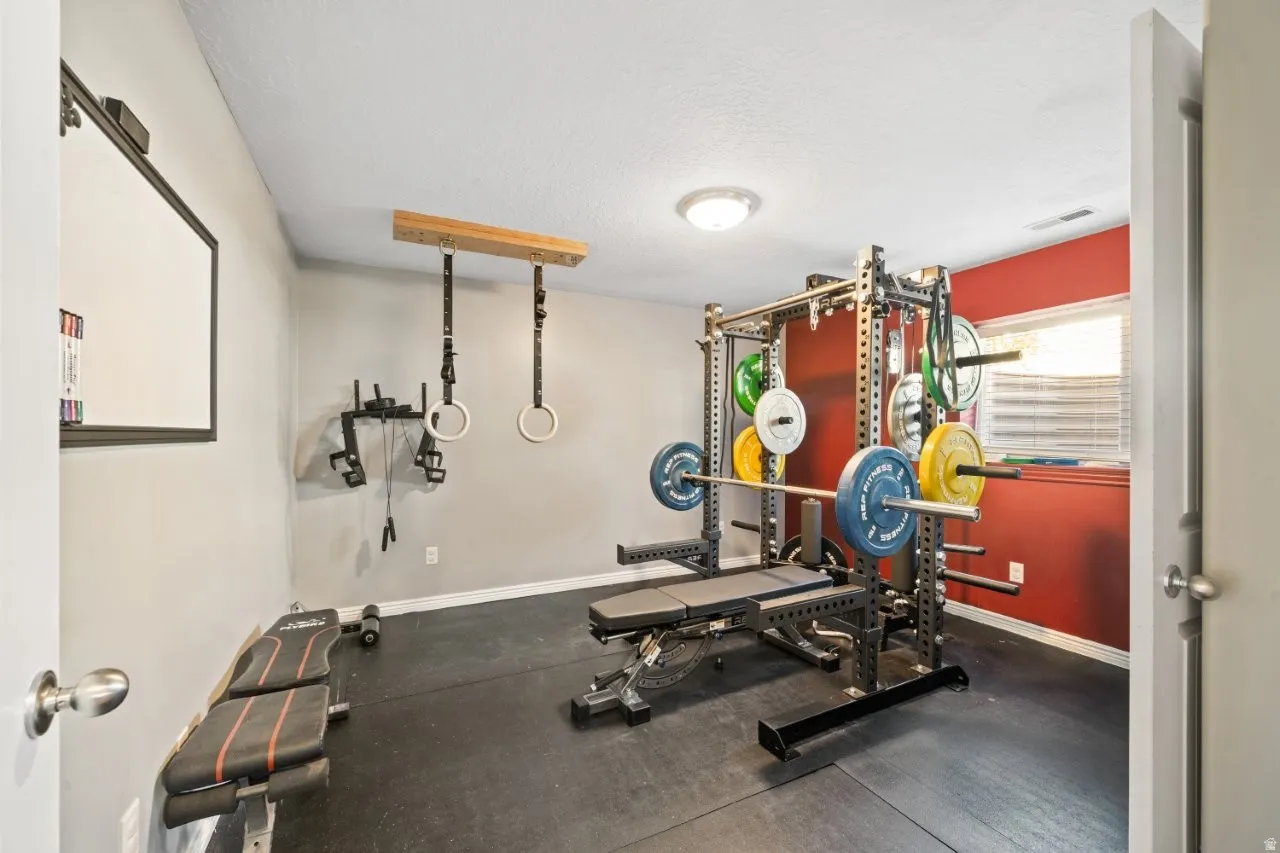 Dedicated fitness space featuring rubber flooring, a flush-mount ceiling light, and a window with blinds