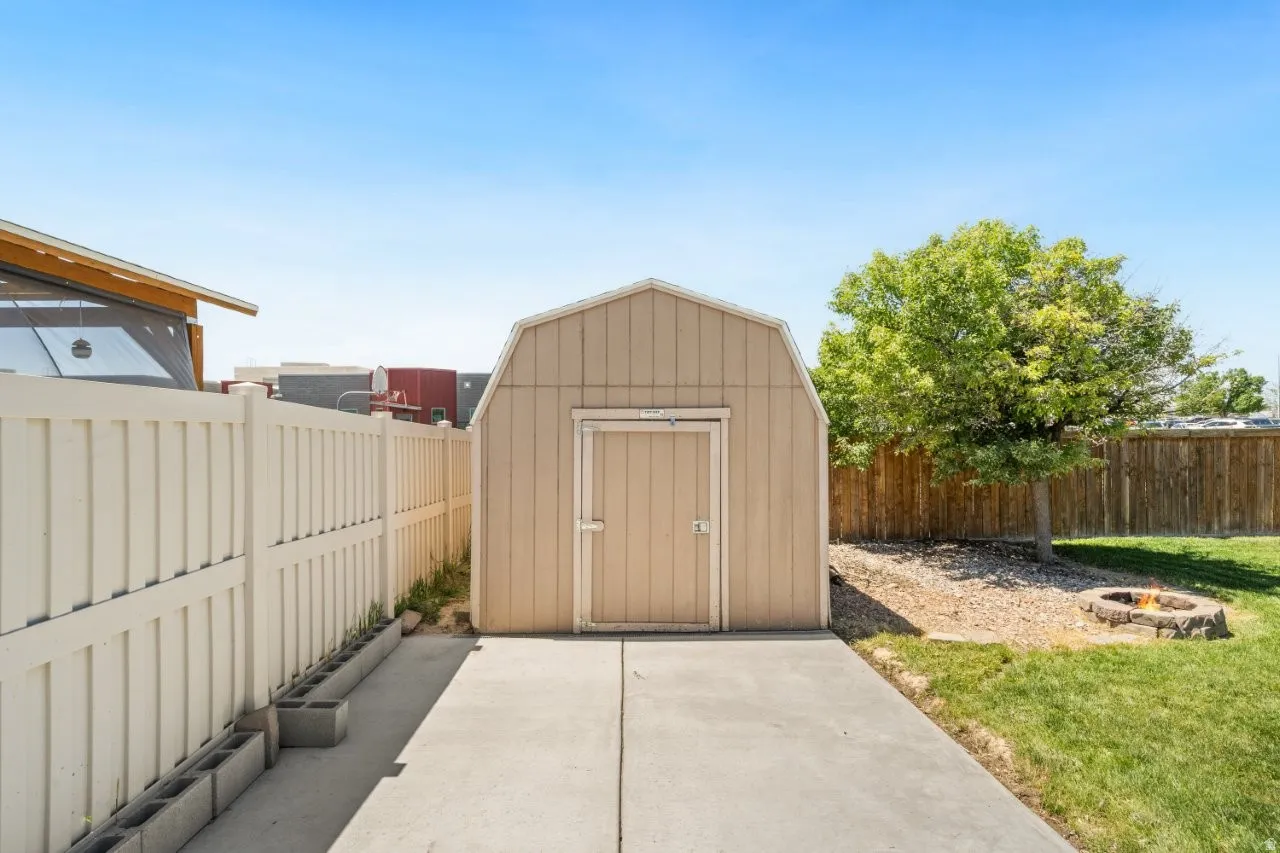 Backyard featuring a light-colored storage shed with a gambrel roof, concrete pad, and a white privacy fence