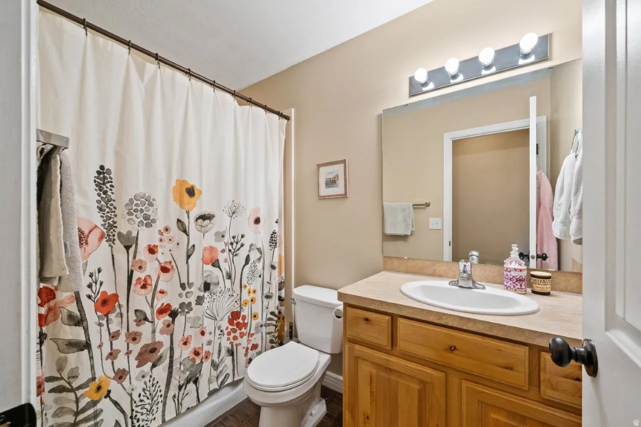 Full bathroom featuring a shower/tub combination with a wall-mounted shower rod, a white toilet, a wood-finish vanity with a built-in sink, and a large wall-mounted mirror with an overhead light fixture