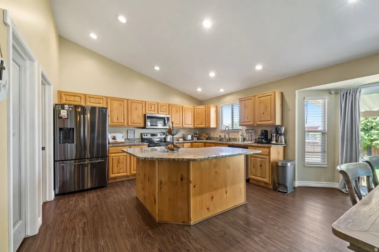 Kitchen featuring a central island with a stone-finish countertop, stainless steel appliances, wood cabinetry, and wood-finish flooring