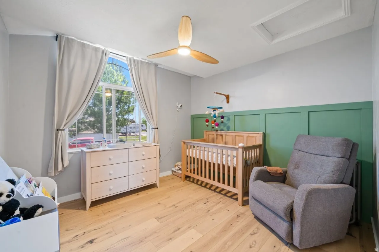 Room featuring wood-finish flooring, a decorative green wainscoting accent wall, a ceiling fan with integrated lighting, and a large arched window with drapery