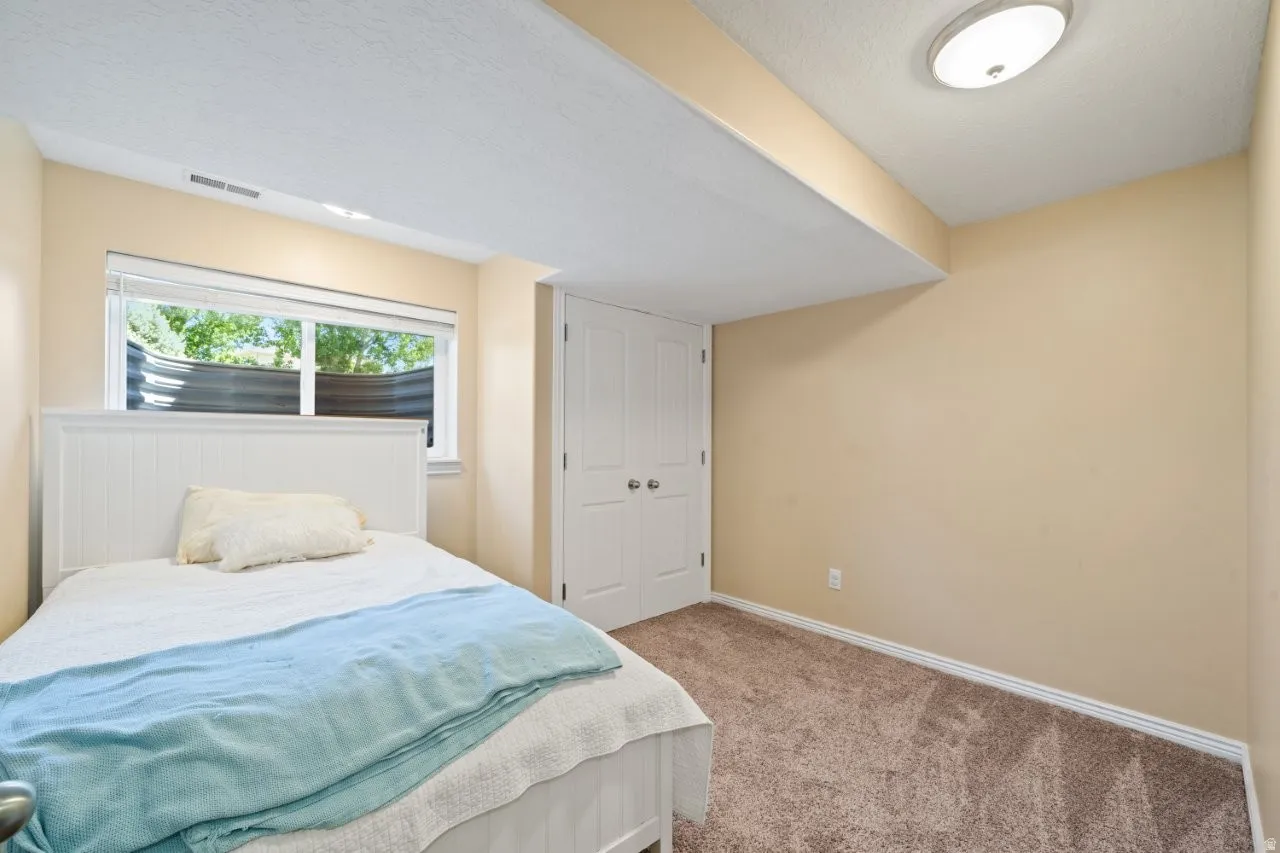 Bedroom featuring a window with natural light, neutral-toned walls, plush carpet flooring, a flush-mount ceiling light, and white paneled doors