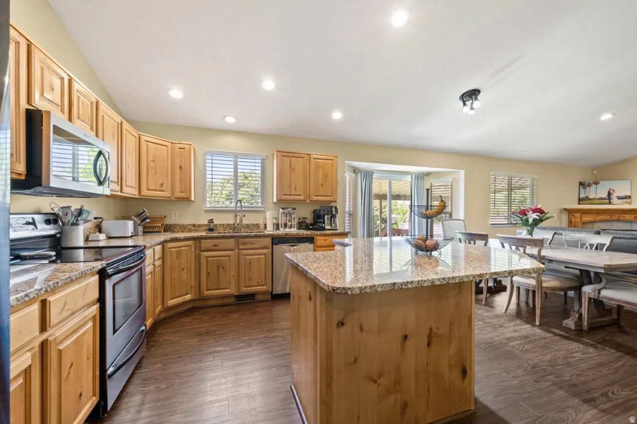 Open-concept kitchen featuring light wood cabinetry, stainless steel appliances, granite countertops, and wood-finish flooring