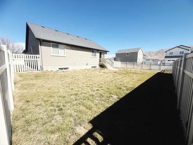 Fenced backyard featuring a beige siding exterior with multiple windows and a rear deck with stairs