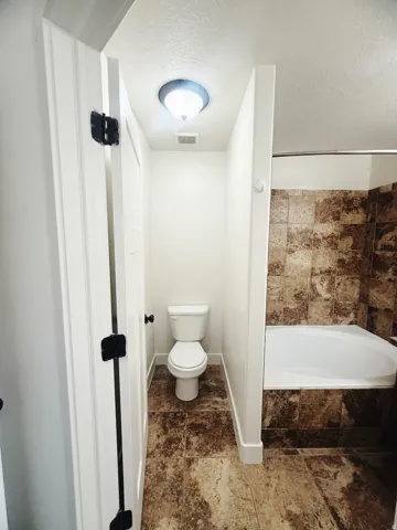Bathroom featuring a white toilet, tile flooring, and a built-in bathtub with tile surround