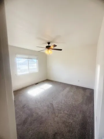 Spacious room featuring neutral carpeting, a large window with blinds, and a ceiling fan with integrated lighting