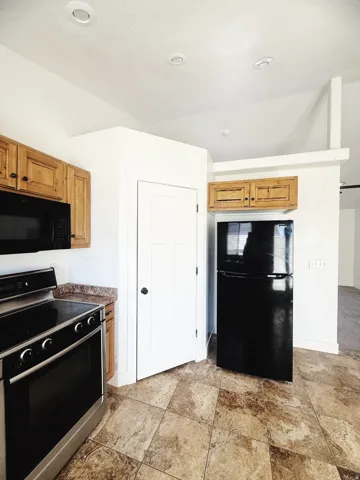 Kitchen featuring tiled flooring, wood cabinetry, a black oven range with a stainless steel front, a black microwave, and a black refrigerator