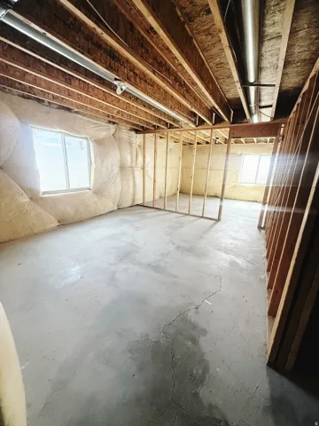 Unfinished basement space featuring exposed wood joists and subflooring, framed walls, and insulated wall sections