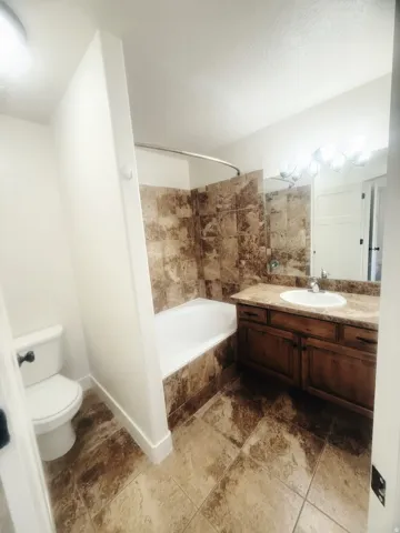 Bathroom featuring a white bathtub, tiled shower surround, a vanity with a drop-in sink, and a commode