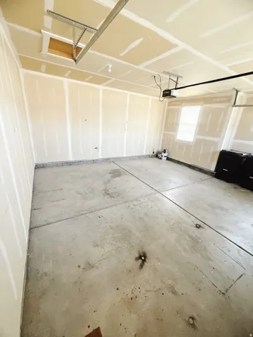 Spacious garage with concrete flooring, exposed drywall, and a ceiling-mounted garage door opener
