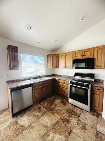 Kitchen featuring warm-toned cabinetry, a stainless steel dishwasher, and a stainless steel range with a black oven