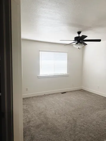 Spacious room featuring neutral carpeting, a ceiling fan with integrated lighting, and a window with blinds