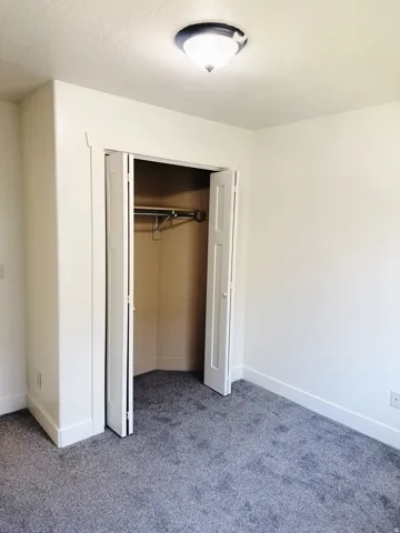 Bedroom featuring plush gray carpeting, white walls, and a bi-fold closet with a built-in hanging rod