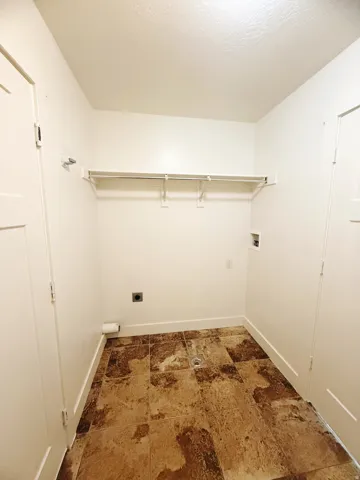 Laundry area featuring large format tile flooring, white walls, and a built-in shelf