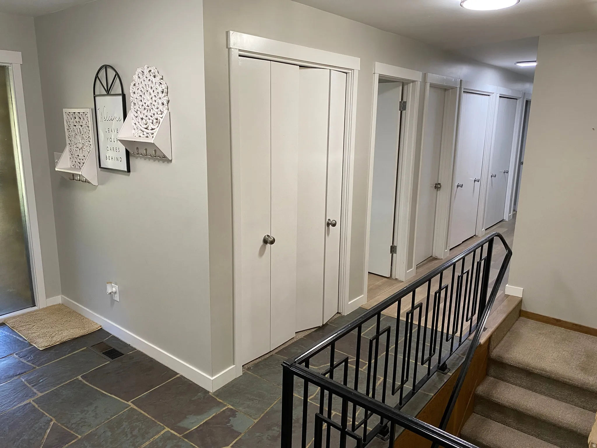 Entryway featuring natural slate flooring, a neutral color palette, white baseboards, and a contemporary black metal stair railing