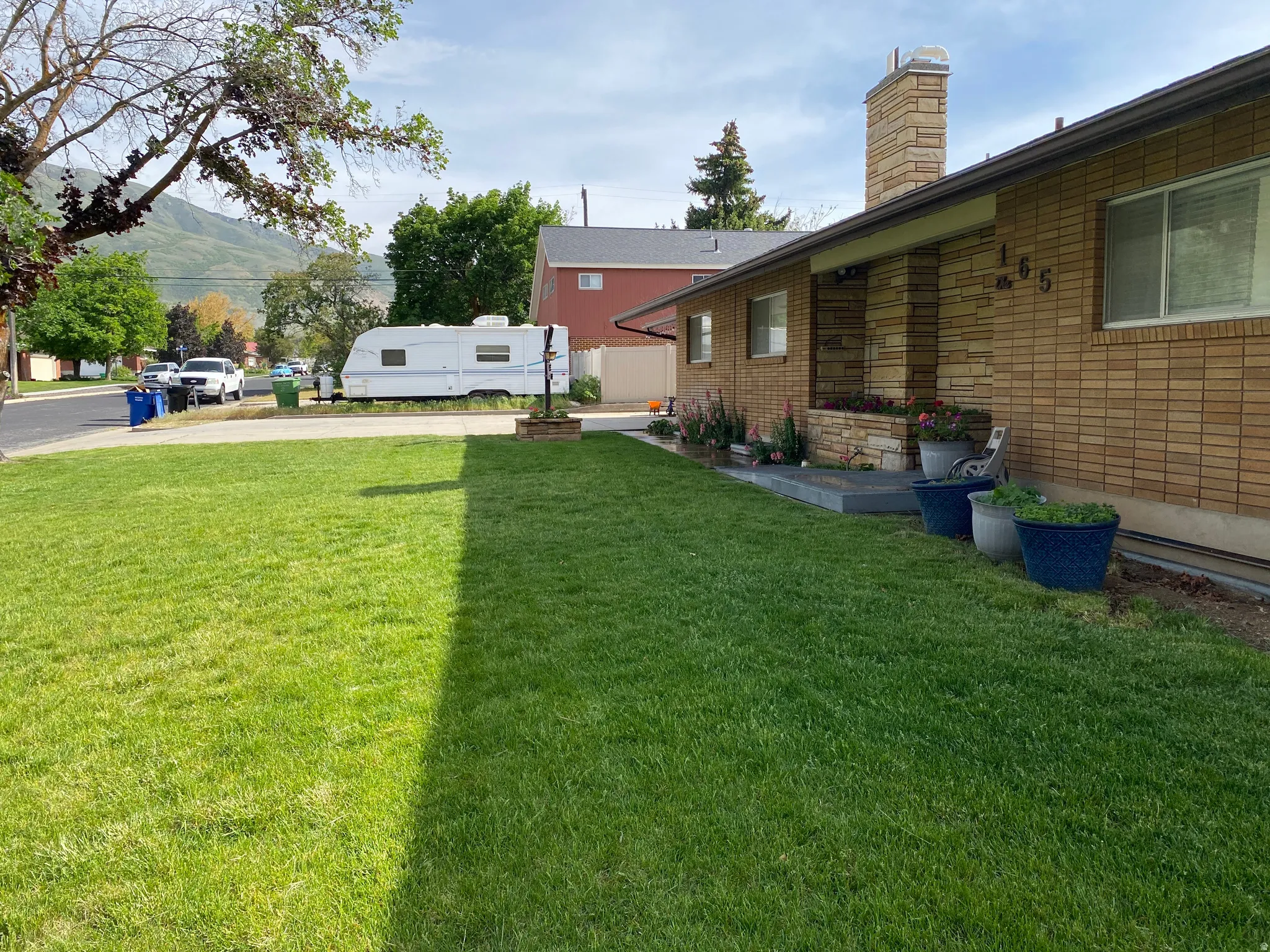 Expansive front lawn with established landscaping, a brick facade, and a stone chimney
