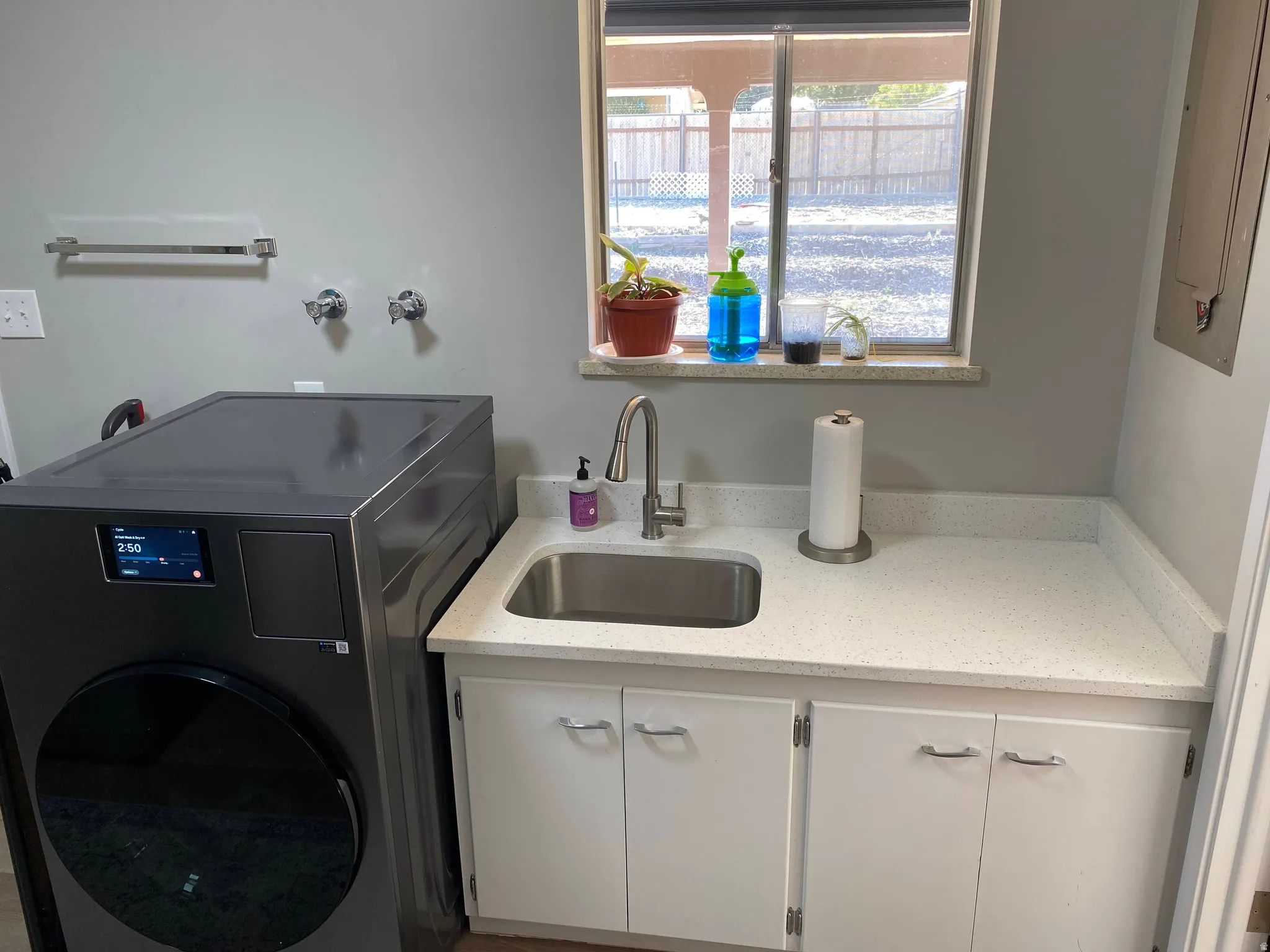 Utility room with a stainless steel sink, speckled white countertop, and white cabinetry featuring chrome hardware