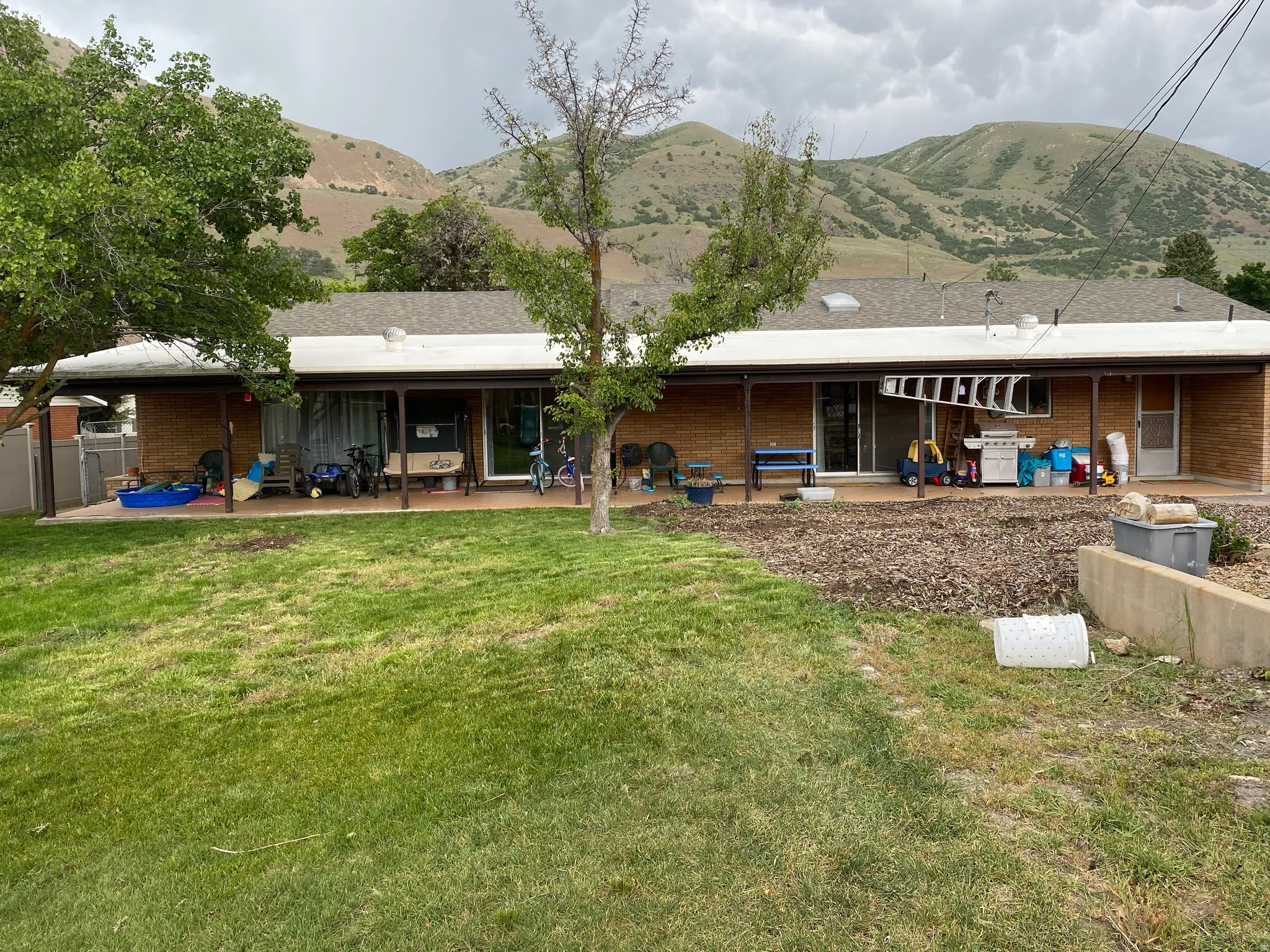 Expansive green lawn with mature trees and a covered patio featuring a brick exterior