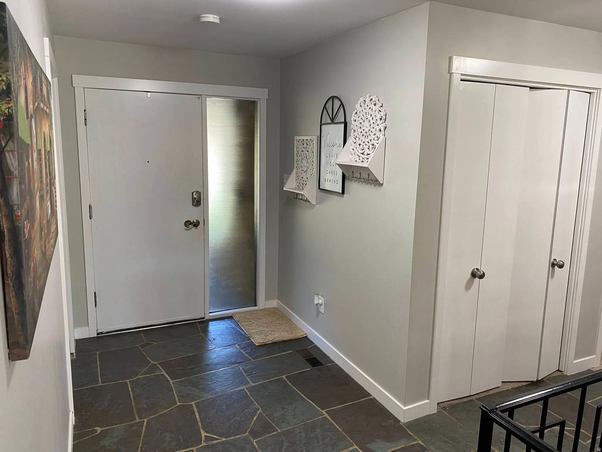 Entryway featuring flagstone flooring, a solid white entry door, an adjacent frosted glass sidelight, and white bi-fold closet doors