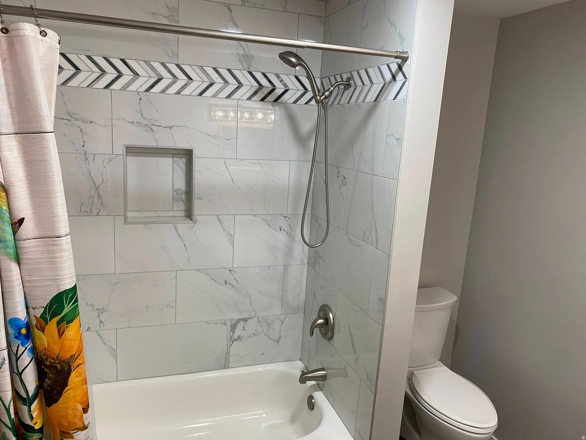 White subway tile shower surround with a decorative chevron accent band, recessed niche, and brushed nickel fixtures
