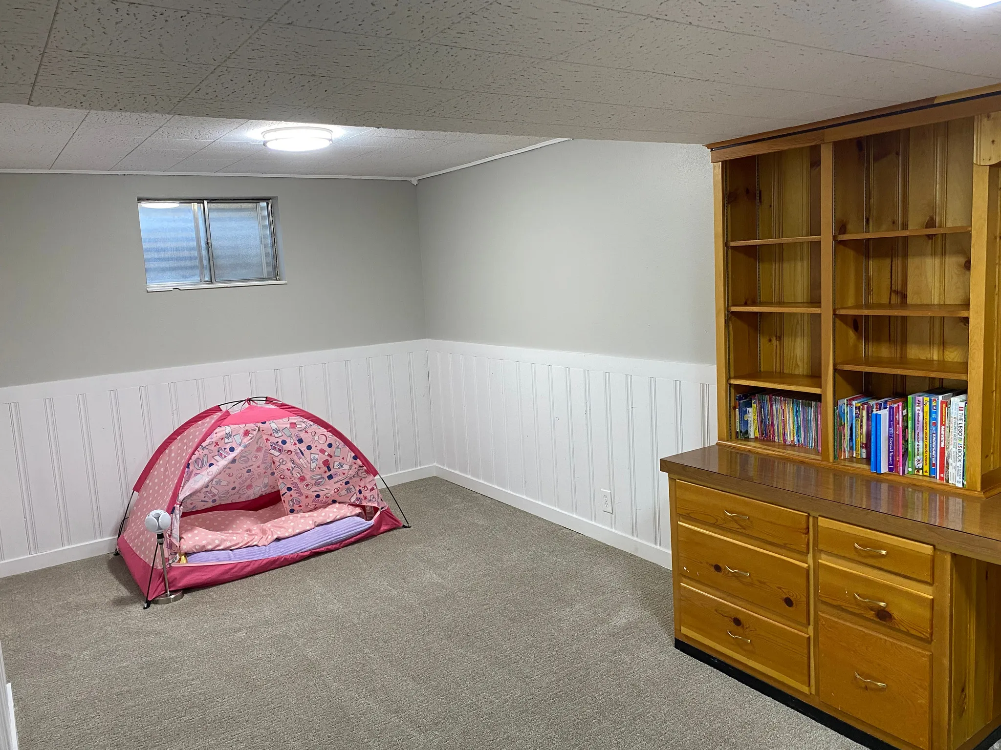 Finished room featuring gray carpet, white wainscoting, a light gray wall, and a built-in wood-finish desk with shelves