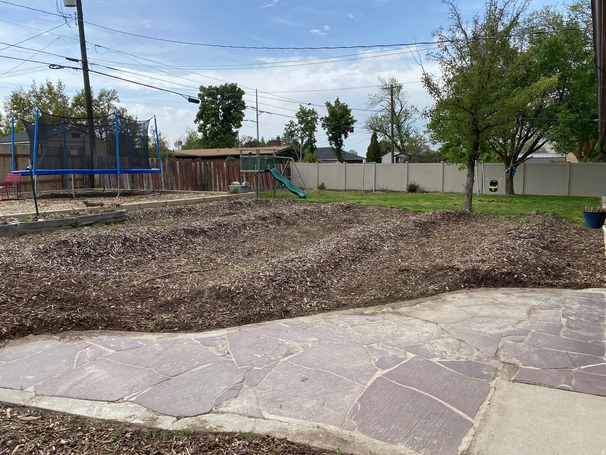 Expansive backyard featuring a flagstone patio, mature tree, wood chip landscaping, and a fenced perimeter