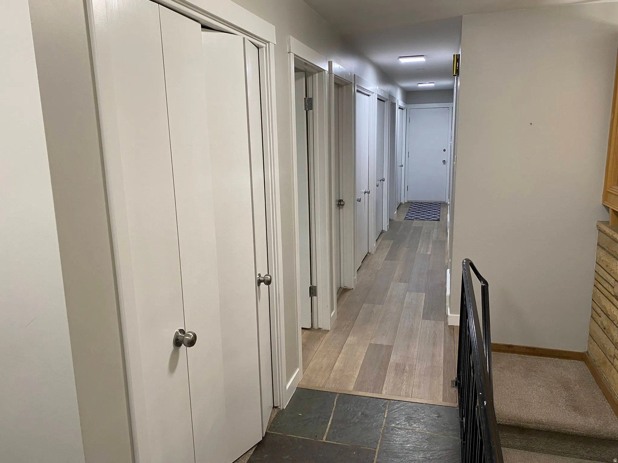 Hallway featuring multiple storage closets with bifold doors, light wood-finish flooring, and recessed ceiling lighting