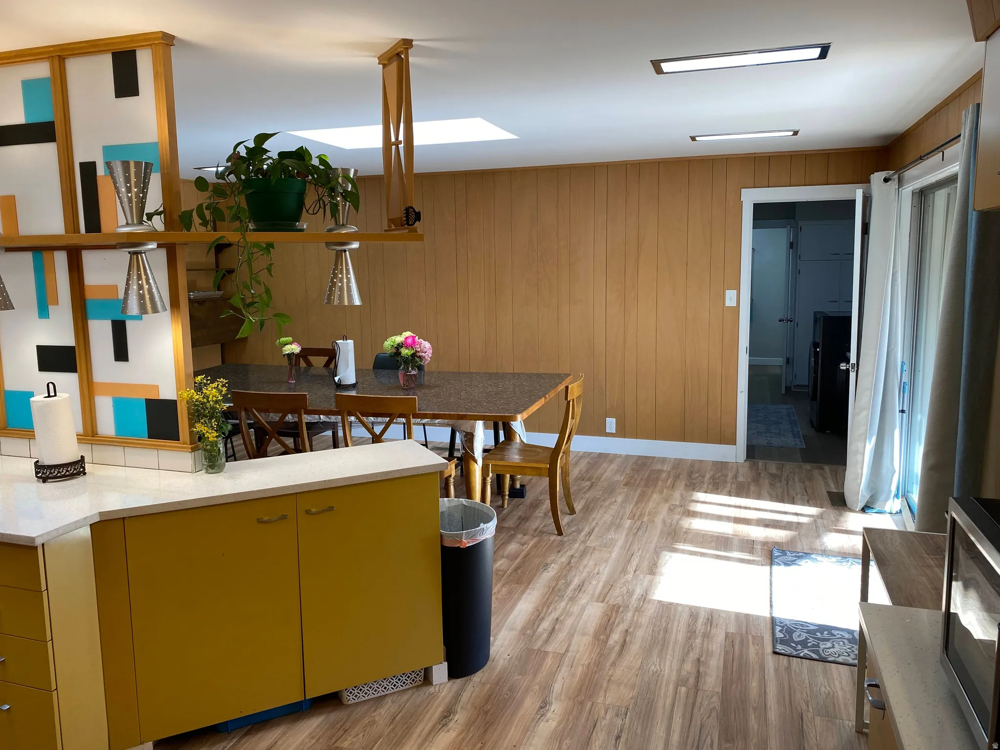 Kitchen and dining area featuring wood-finish flooring, wood-paneled walls, and a recessed skylight