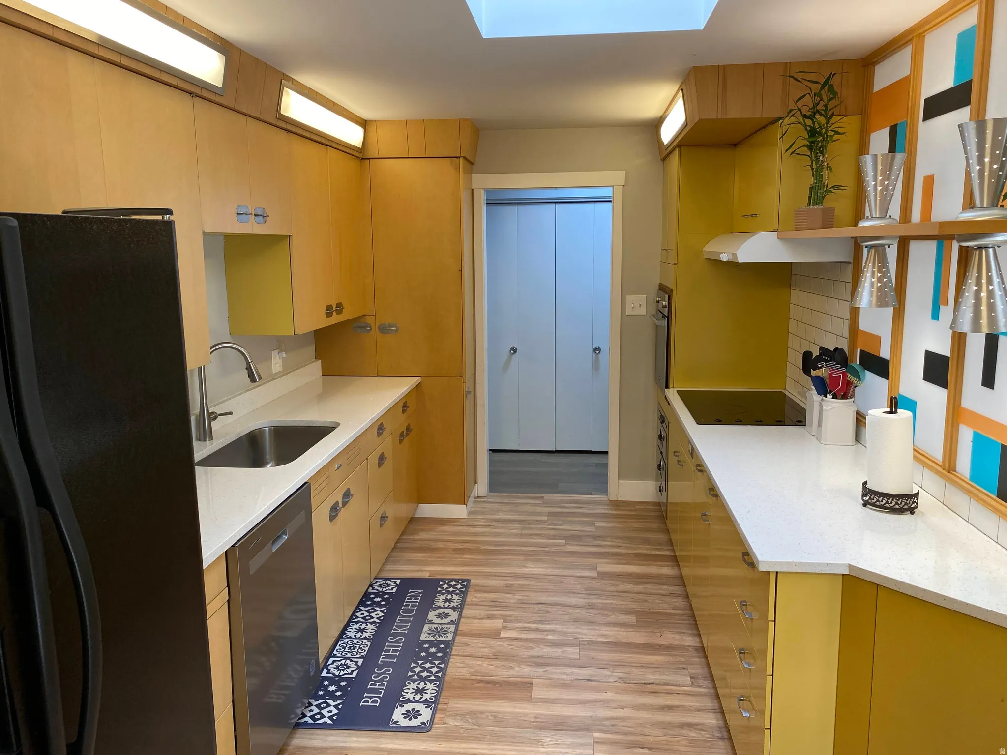 Kitchen featuring wood-finish flooring, light wood cabinetry, white countertops, and a skylight