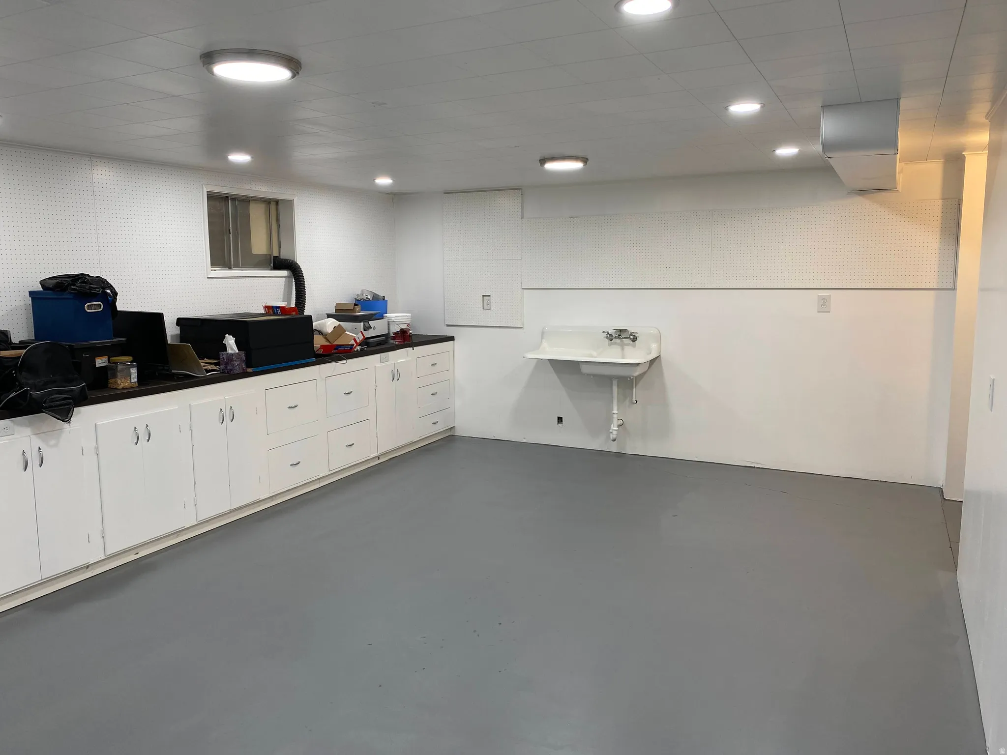 Spacious utility room featuring extensive built-in cabinetry, durable flooring, a utility sink, and ample overhead lighting